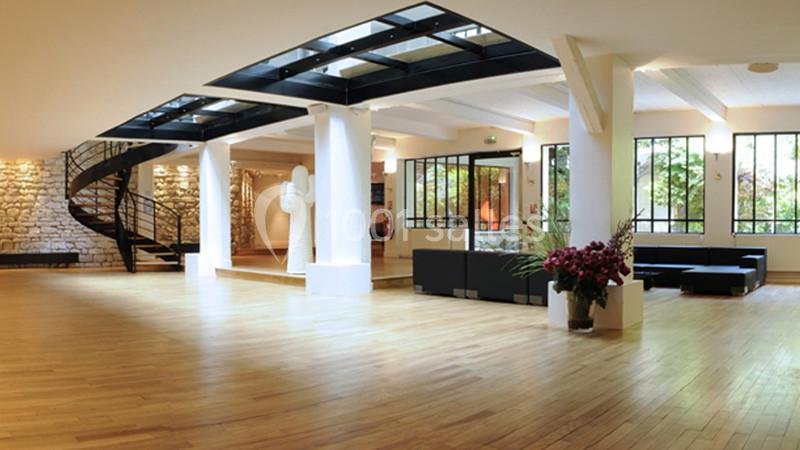 Salle lumineuse avec parquet en bois, escalier en colimaçon, grandes fenêtres et mobilier moderne.