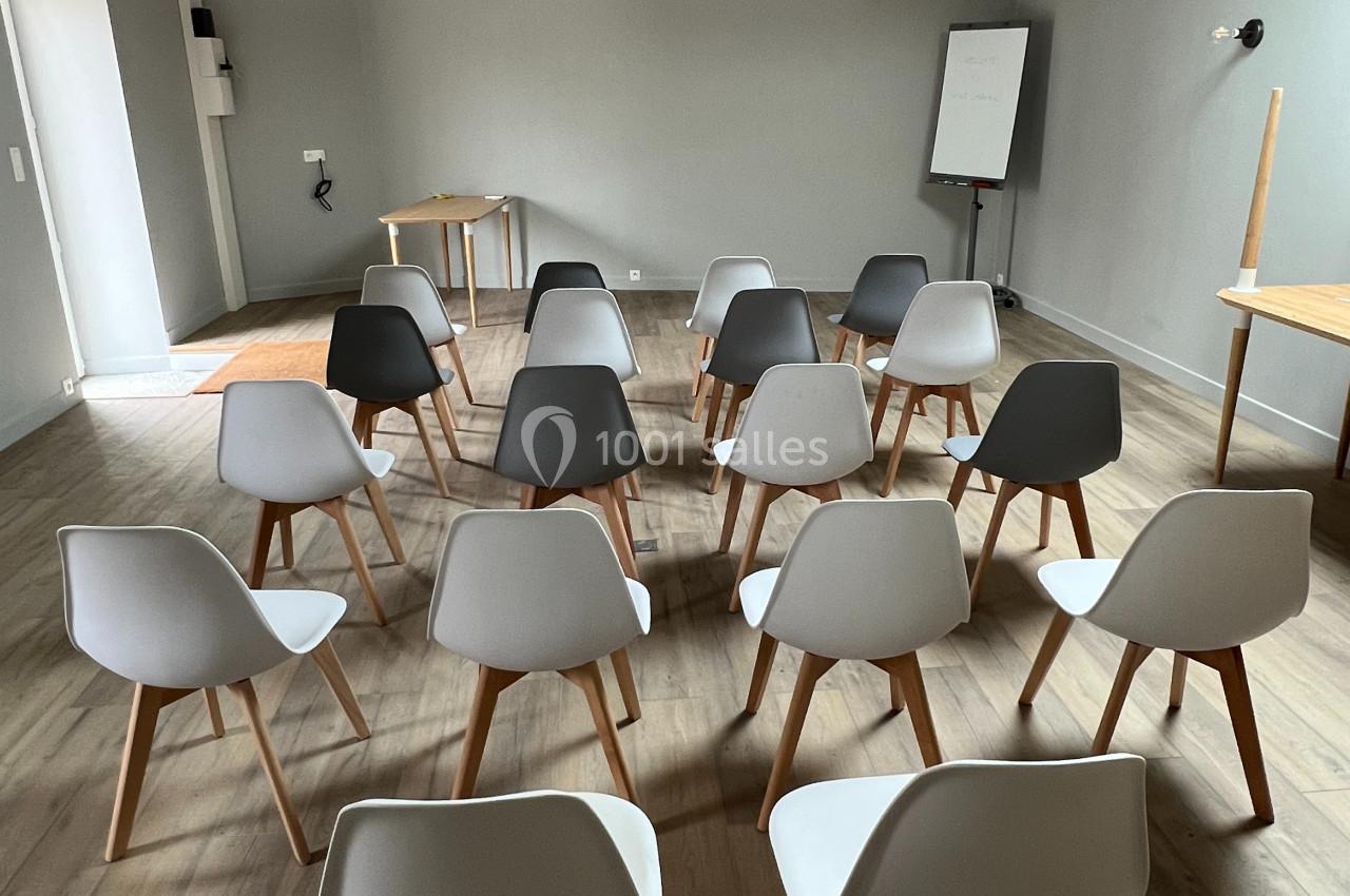 Salle de réunion avec des chaises modernes disposées en rangées face à un tableau blanc et une table en bois.