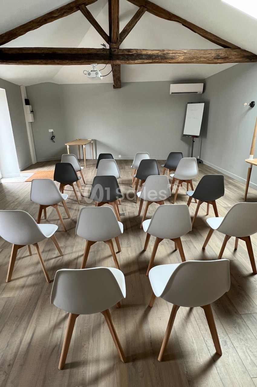 Salle de réunion avec des chaises modernes disposées en rangées face à un tableau blanc et une table en bois.