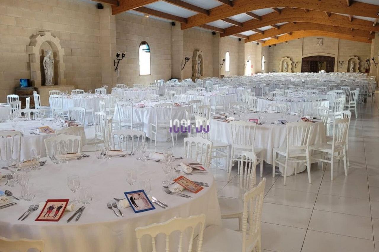 Salle de réception lumineuse avec tables rondes dressées, nappes blanches et chaises en bois clair.