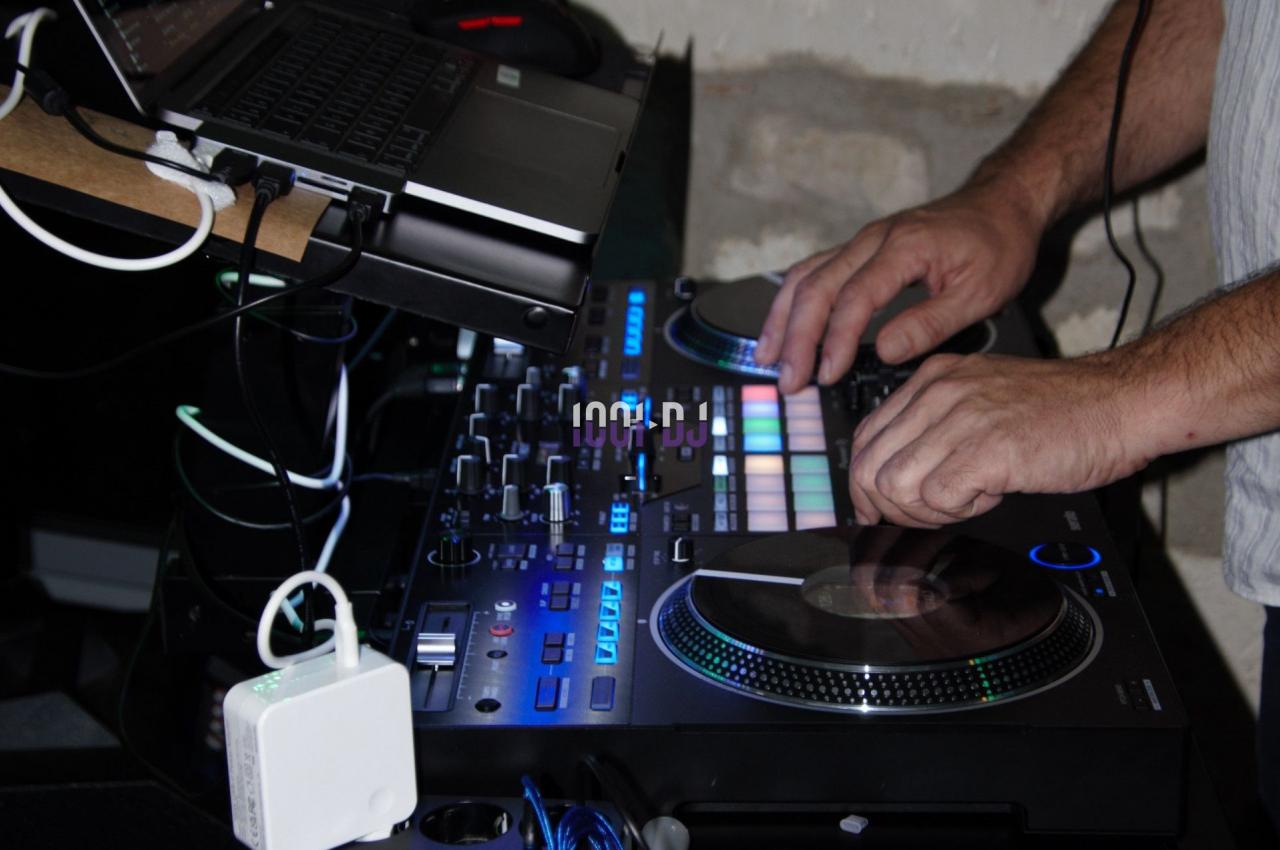 Un DJ manipule une table de mixage équipée de lumières colorées, avec un ordinateur portable posé dessus.
