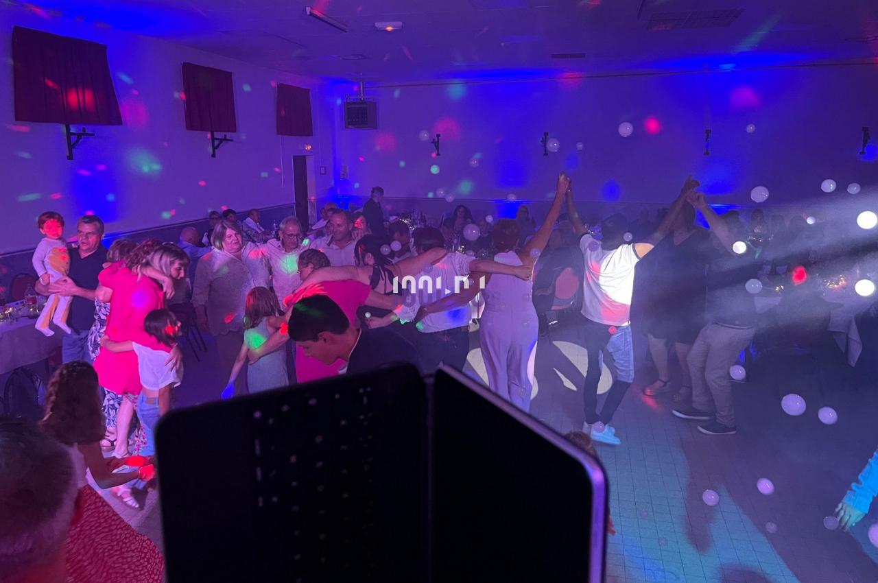 Des personnes dansent en cercle dans une salle éclairée par des lumières colorées lors d'une fête.