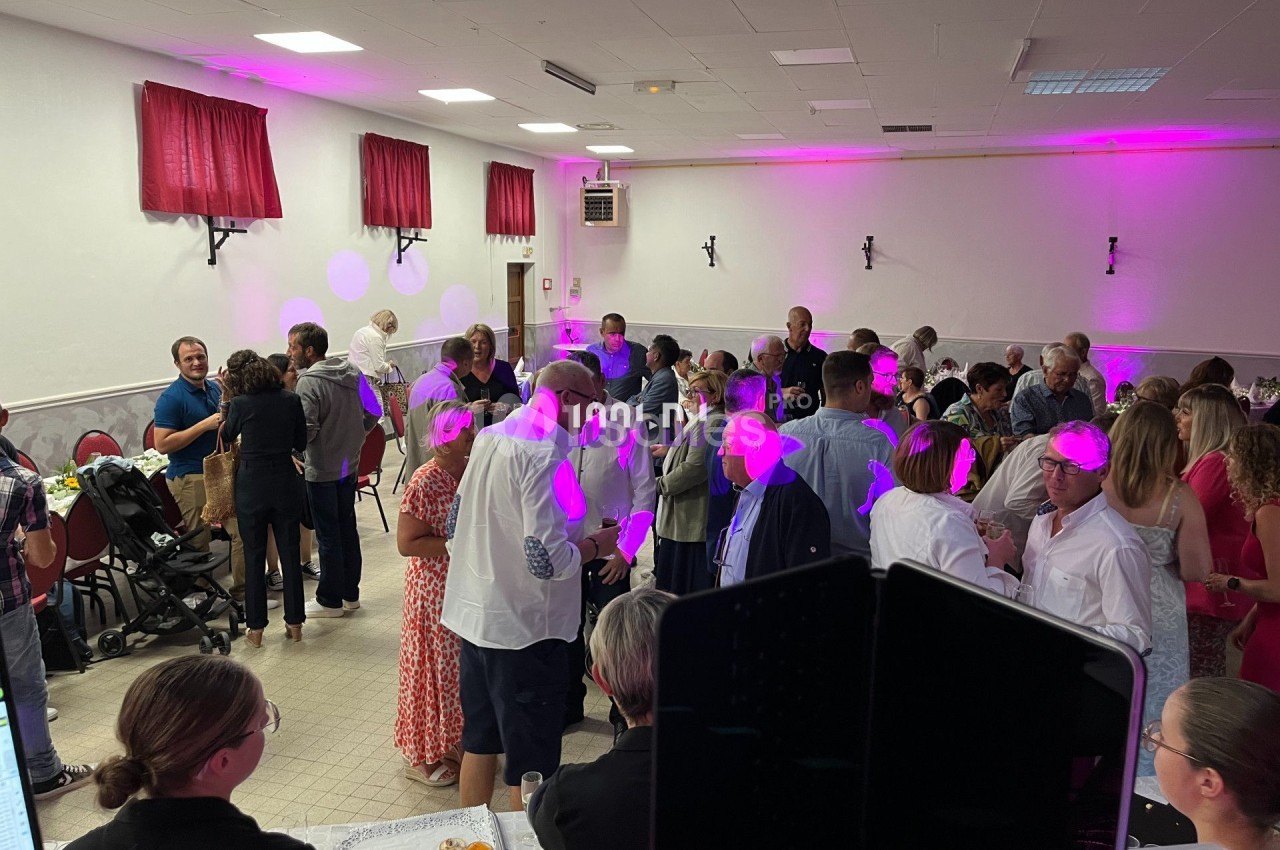 Des personnes discutent et dansent dans une salle éclairée par des lumières roses, lors d'un événement festif.