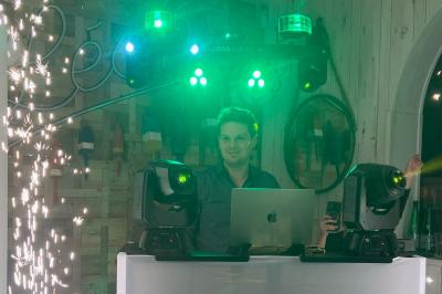 Miniature DJ Coulogne (Pas-de-Calais) - GreG évènements #14 Un DJ mixe sur un ordinateur portable, entouré de lumières colorées dans un décor en bois avec des bouées suspendues.