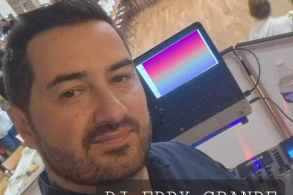 Homme près d'un ordinateur portable et d'un équipement audio dans une salle avec des tables en arrière-plan.