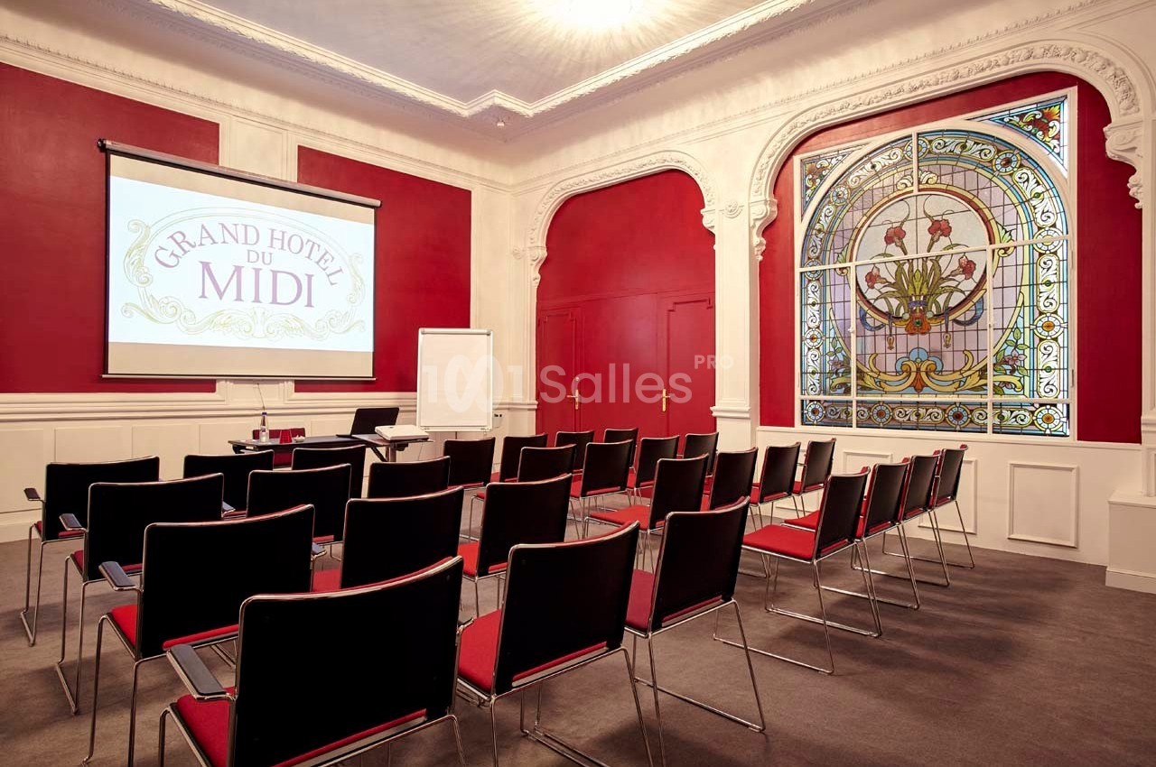 Salle de réunion avec chaises alignées, écran de projection, tableau blanc et vitrail décoratif en arrière-plan.