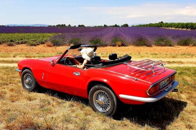 Voiture décapotable rouge garée dans un champ de lavande sous un ciel dégagé.