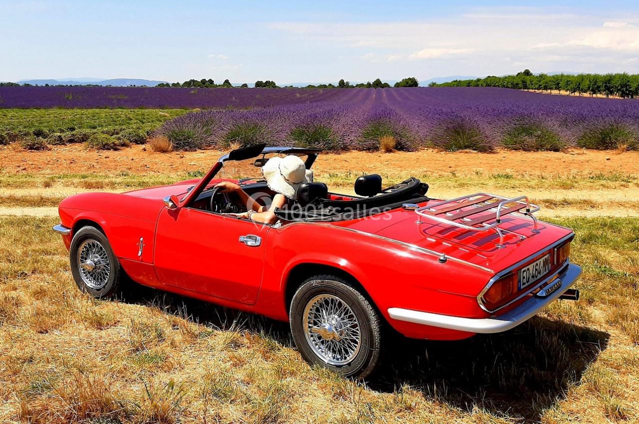 Voiture décapotable rouge garée dans un champ de lavande sous un ciel dégagé.