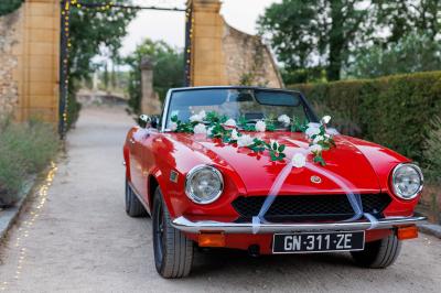 Voiture décapotable classique beige stationnée sur une allée gravillonnée entourée de haies vertes.