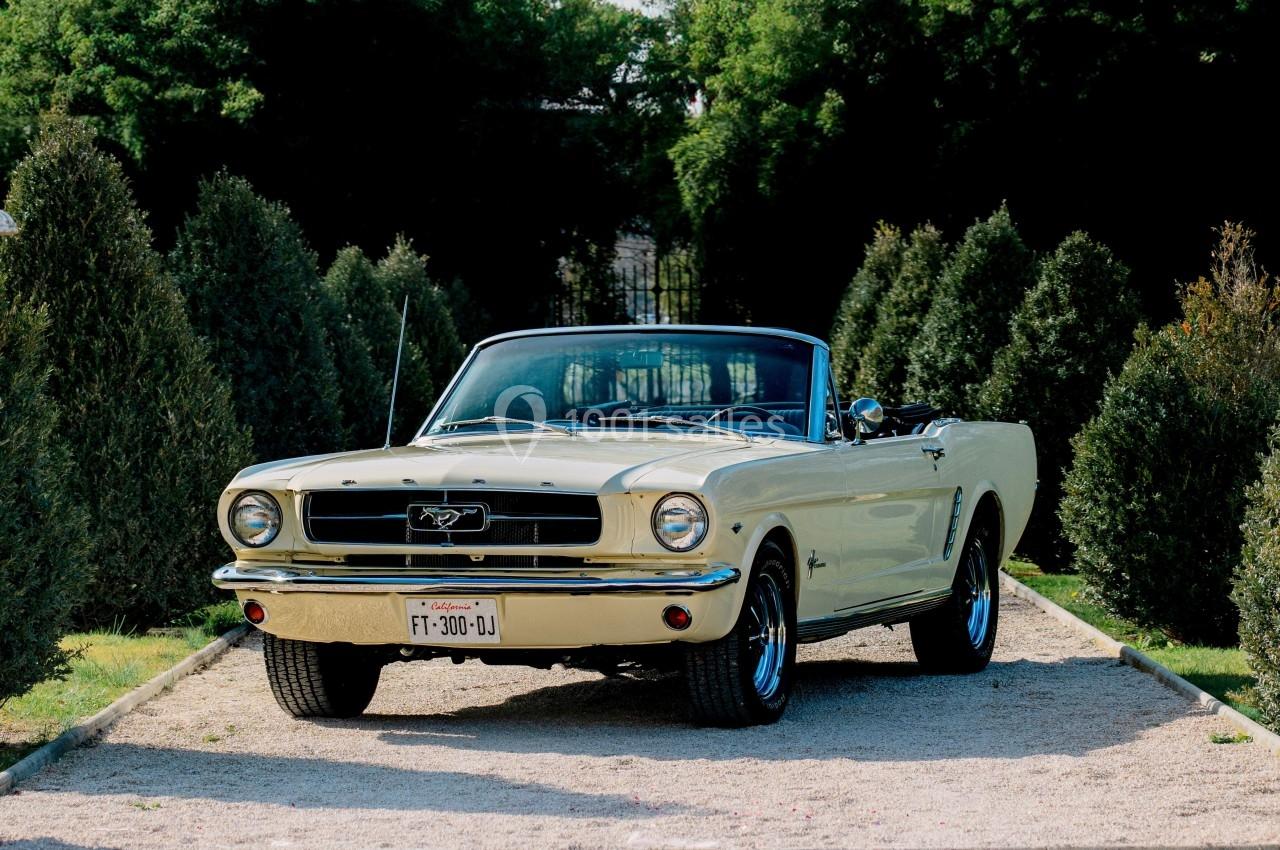 Voiture décapotable classique beige stationnée sur une allée gravillonnée entourée de haies vertes.