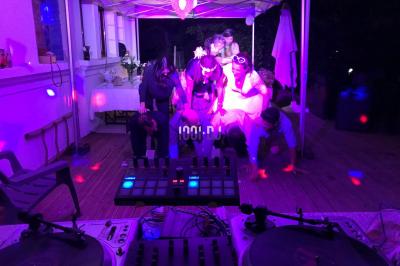 Deux platines vinyles et une table de mixage installées en extérieur sous des parasols, avec des tables en arrière-plan.