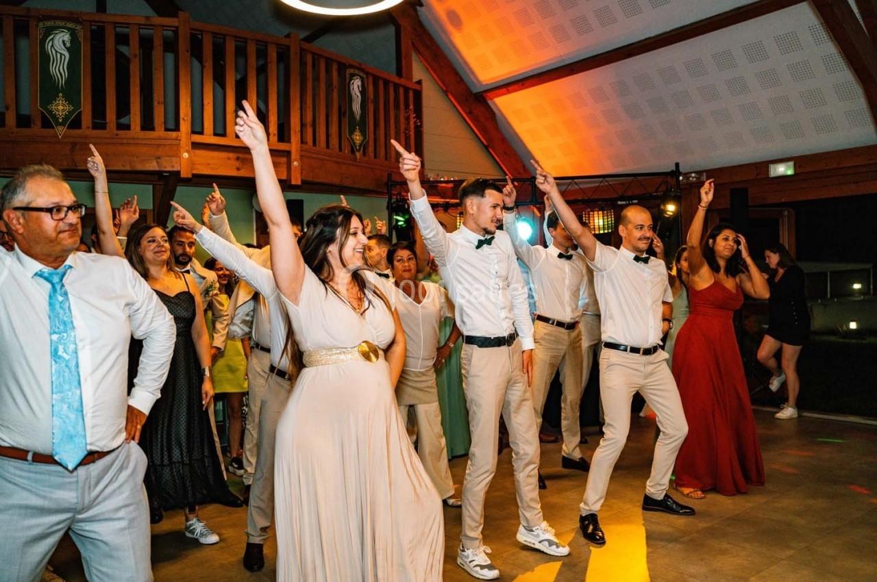 Des personnes dansent en groupe dans une salle éclairée, certaines en tenue de cérémonie.