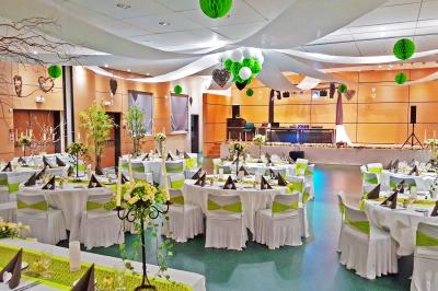 Salle de réception décorée avec des tables rondes, nappes blanches, chaises transparentes et guirlandes lumineuses.