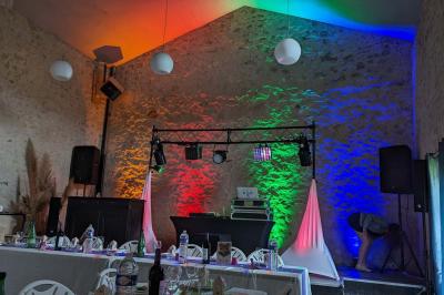 Salle de réception décorée avec des tables rondes, nappes blanches, chaises transparentes et guirlandes lumineuses.