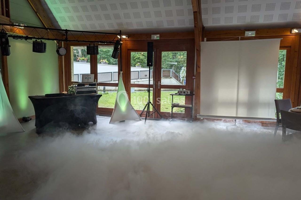 Salle de réception avec éclairage d'ambiance, fumée au sol et vue sur un espace extérieur verdoyant.