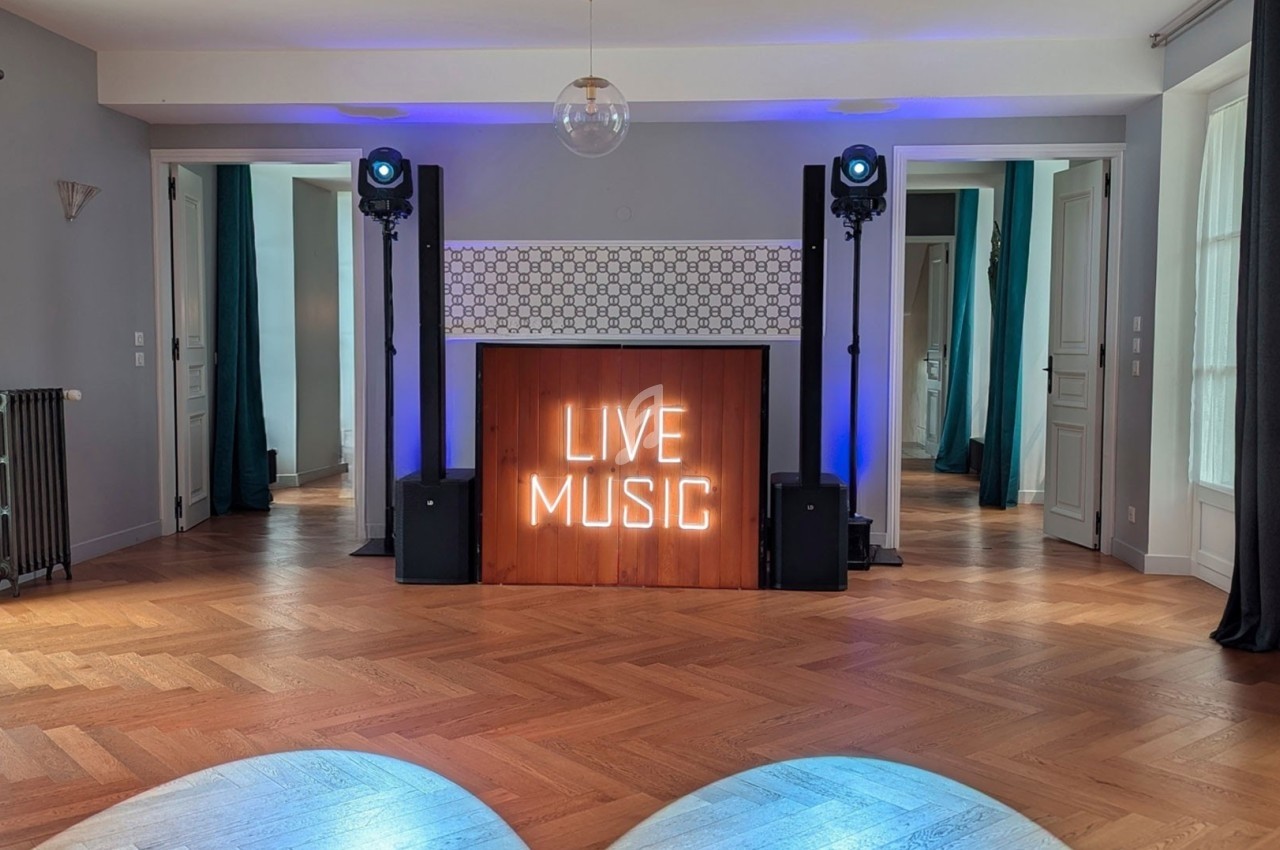 Salle avec parquet, éclairage bleu, panneau lumineux ’Live Music’ et équipements audio sur pied.