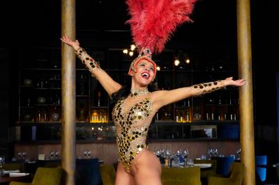 Femme portant une tenue rouge ornée de perles et un accessoire de tête assorti, posant devant une porte en bois sculpté.