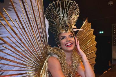 Femme portant une tenue rouge ornée de perles et un accessoire de tête assorti, posant devant une porte en bois sculpté.