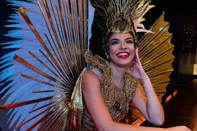 Femme portant une tenue rouge ornée de perles et un accessoire de tête assorti, posant devant une porte en bois sculpté.