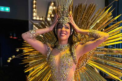 Femme portant une tenue rouge ornée de perles et un accessoire de tête assorti, posant devant une porte en bois sculpté.