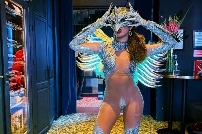 Femme portant une tenue rouge ornée de perles et un accessoire de tête assorti, posant devant une porte en bois sculpté.