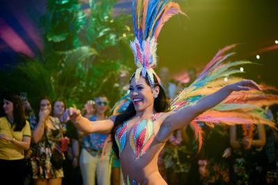 Femme portant une tenue rouge ornée de perles et un accessoire de tête assorti, posant devant une porte en bois sculpté.