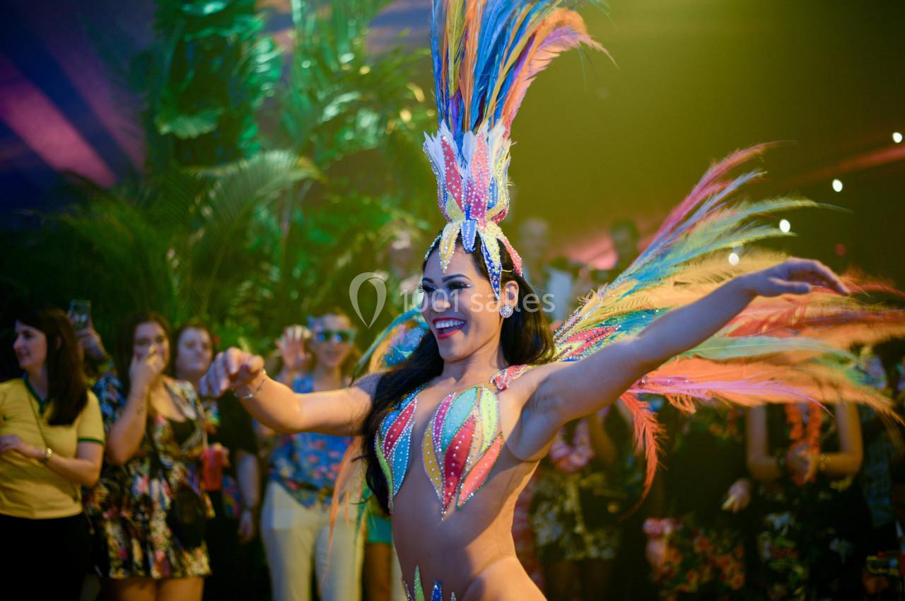 Danseuse en costume coloré avec plumes, exécutant un mouvement devant un public lors d'un événement festif.