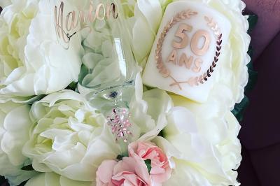 Flûte personnalisée avec le prénom ’Marion’ et bougie marquée ’50 ans’, posées sur une table devant un fond rose.