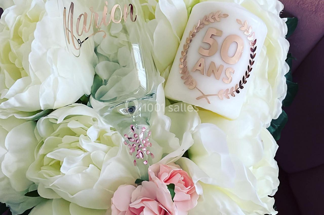 Bouquet de fleurs blanches et roses avec une flûte gravée et une bougie marquée ’50 ans’.