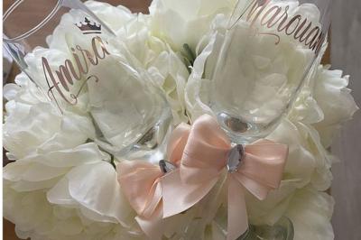 Flûte personnalisée avec le prénom ’Marion’ et bougie marquée ’50 ans’, posées sur une table devant un fond rose.