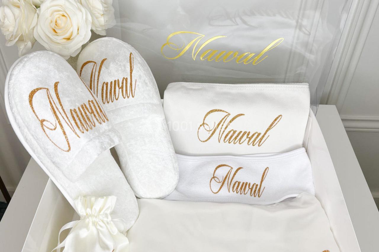 Coffret contenant des articles personnalisés avec le prénom ’Nawal’ : serviettes, chaussons, pochette et boîte transparente.