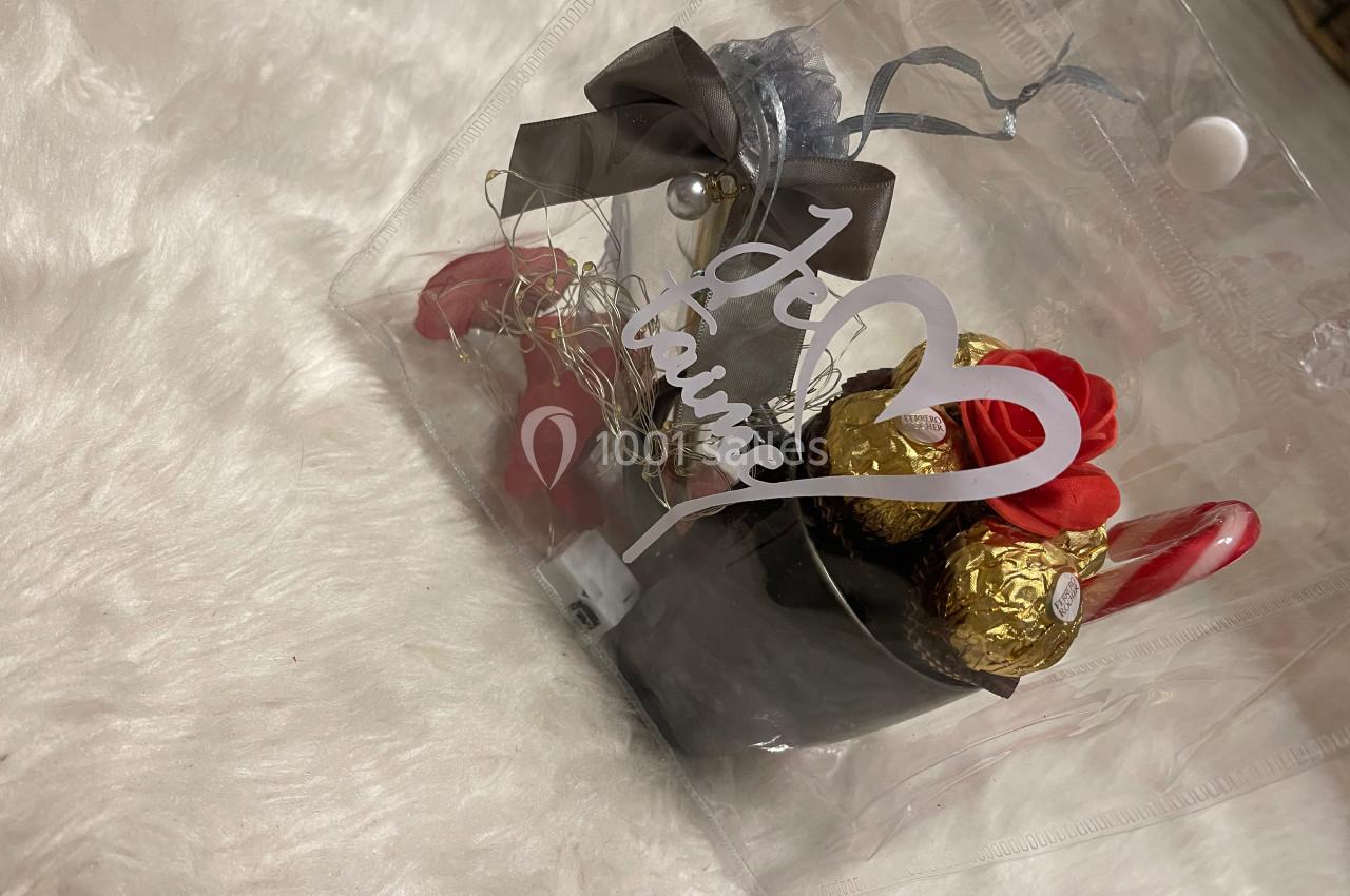 Petit panier cadeau transparent contenant des chocolats, des roses rouges artificielles et un ruban avec l'inscription ’Je t…