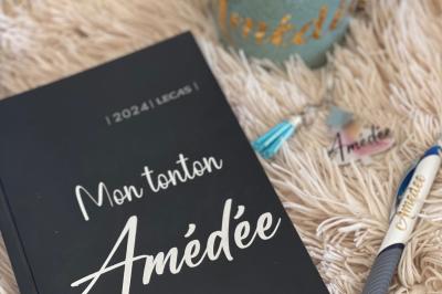 Flûte personnalisée avec le prénom ’Marion’ et bougie marquée ’50 ans’, posées sur une table devant un fond rose.