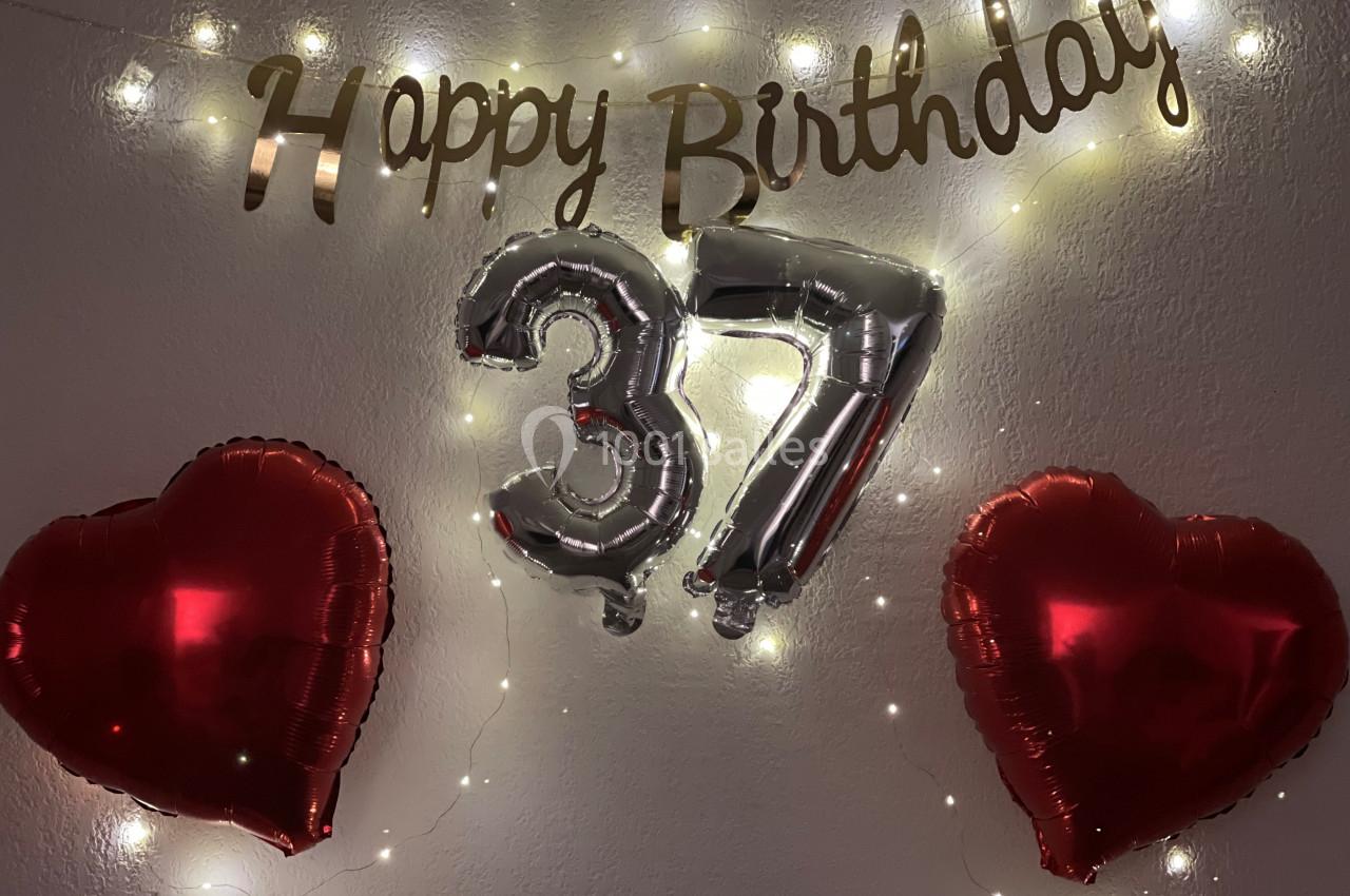 Décoration d'anniversaire avec ballons argentés ’37’, guirlande ’Happy Birthday’ et deux ballons rouges en forme de cœur.