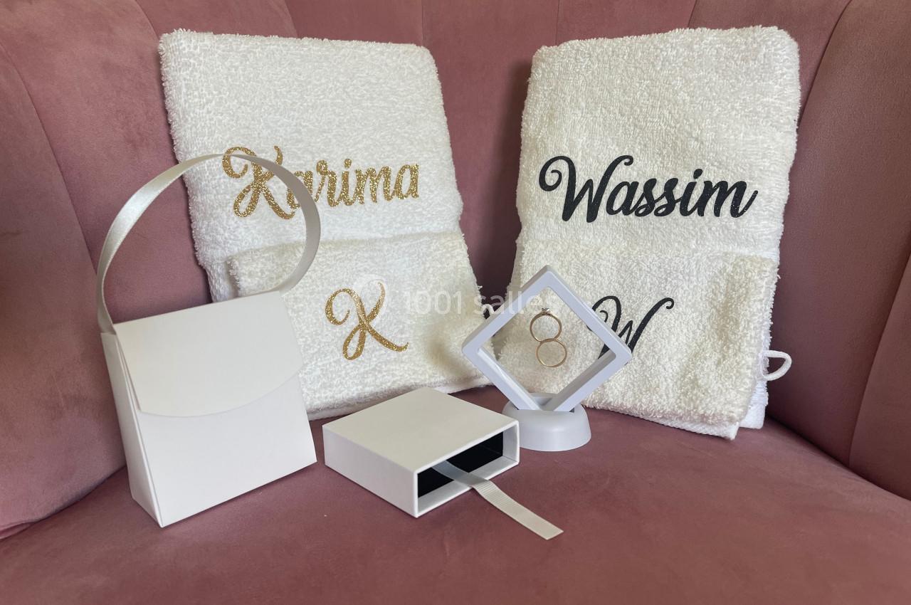 Serviettes personnalisées avec des prénoms brodés, posées sur un fauteuil rose, accompagnées de boîtes blanches.