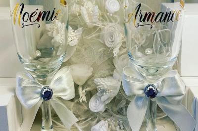 Flûte personnalisée avec le prénom ’Marion’ et bougie marquée ’50 ans’, posées sur une table devant un fond rose.