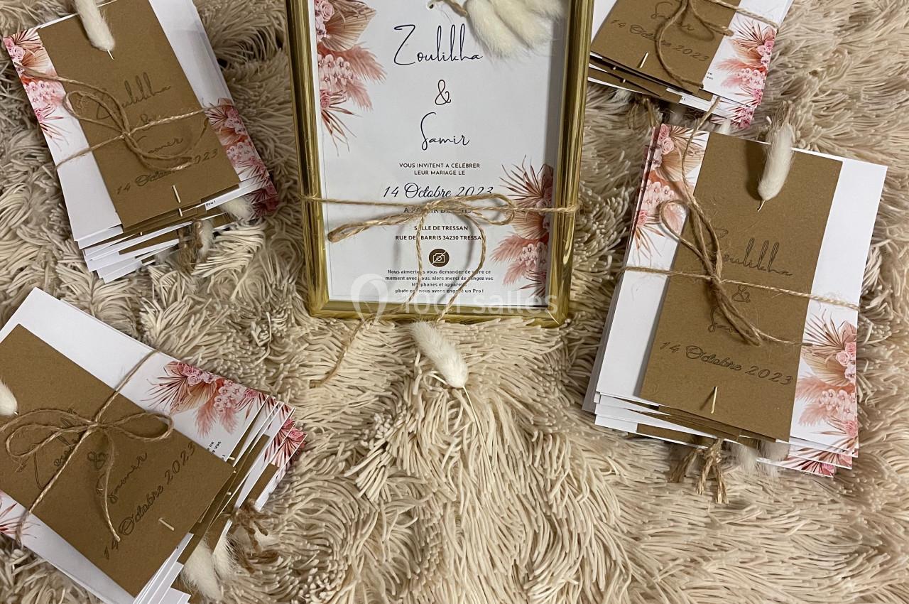 Cartes d'invitation décorées avec des fleurs et des enveloppes kraft, disposées autour d'un cadre doré sur un tapis beige.