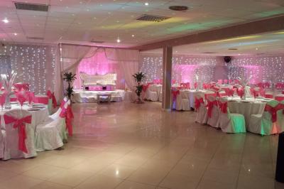 Plusieurs personnes discutent devant un bâtiment avec des voitures garées, dont une voiture rouge sportive.