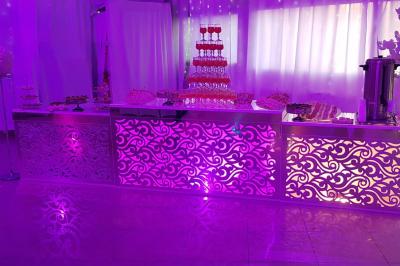 Plusieurs personnes discutent devant un bâtiment avec des voitures garées, dont une voiture rouge sportive.