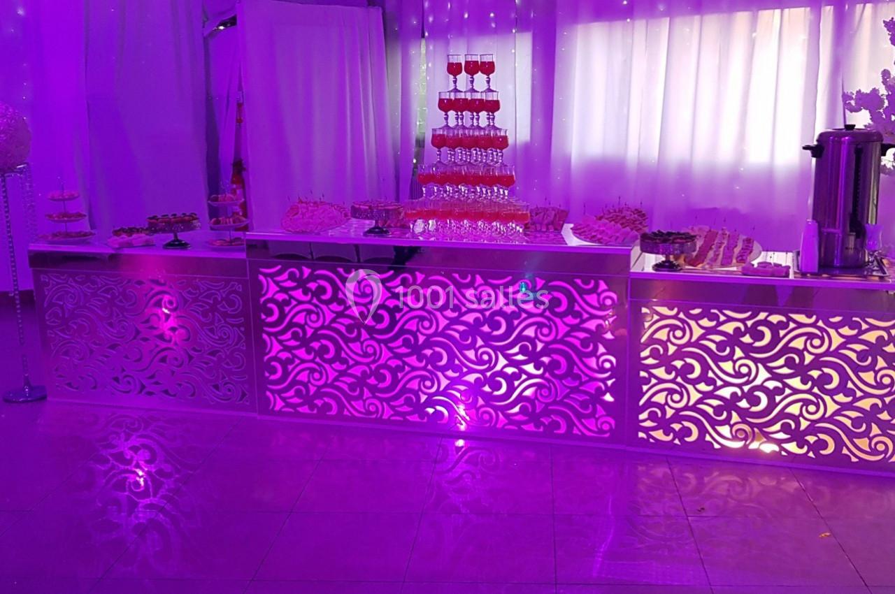 Buffet décoratif éclairé en violet avec des desserts variés et une fontaine à boissons en arrière-plan.