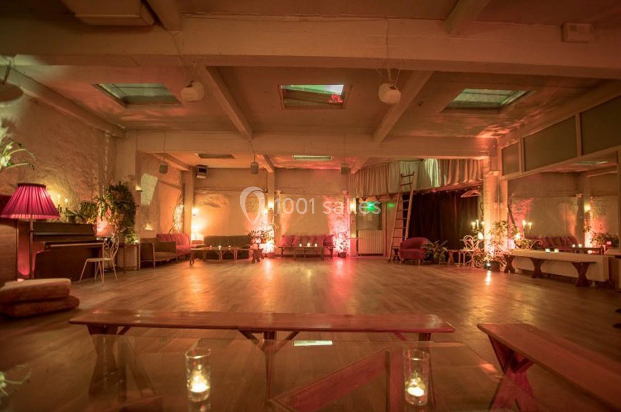 Salle spacieuse avec parquet, éclairage tamisé, plantes et mobilier confortable, ambiance chaleureuse et accueillante.