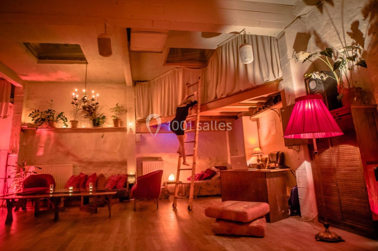 Intérieur chaleureux avec éclairage tamisé, canapé, plantes et mezzanine accessible par une échelle en bois.