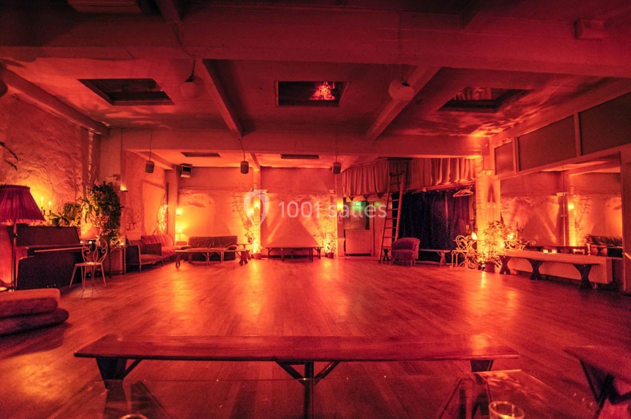 Salle spacieuse à l'éclairage tamisé rouge-orange, avec bancs, plantes et ambiance chaleureuse.