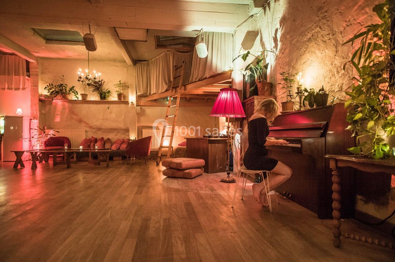 Une femme joue du piano dans une pièce chaleureuse avec éclairage tamisé, plantes et mobilier en bois.