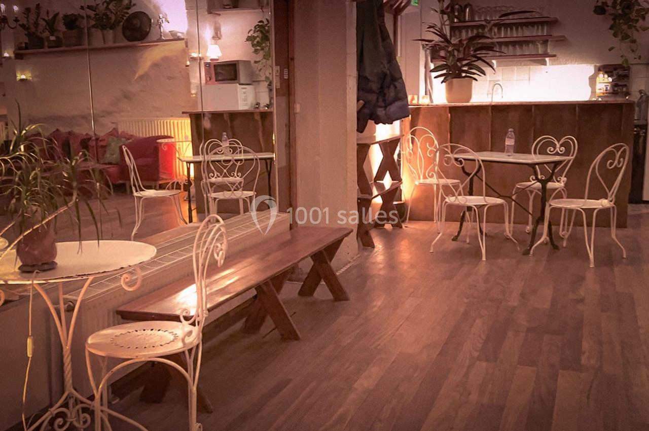 Salle chaleureuse avec tables et chaises en fer forgé, plantes décoratives et éclairage tamisé.