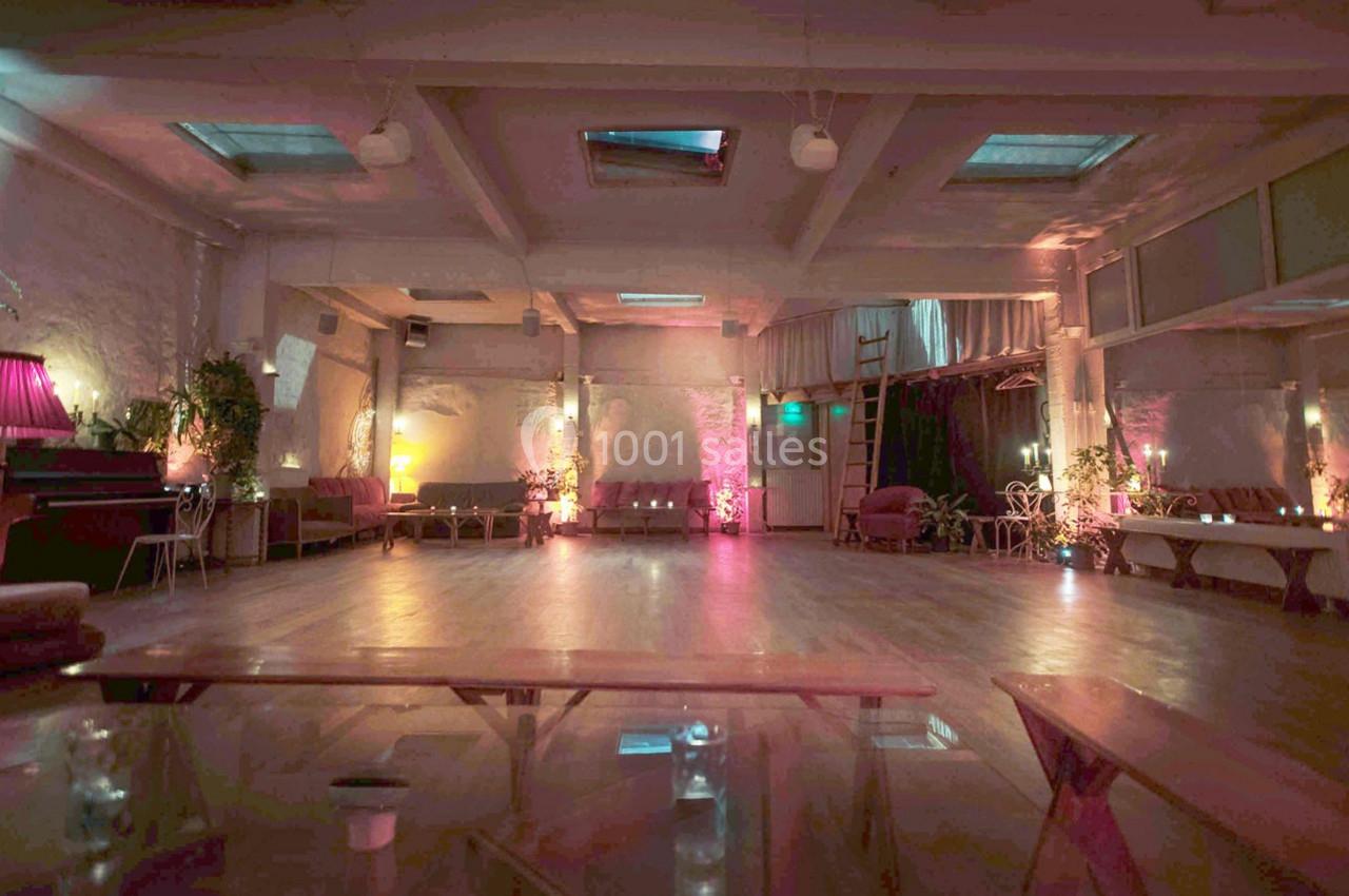 Salle spacieuse avec parquet, éclairage tamisé coloré, canapés et plantes disposés le long des murs.