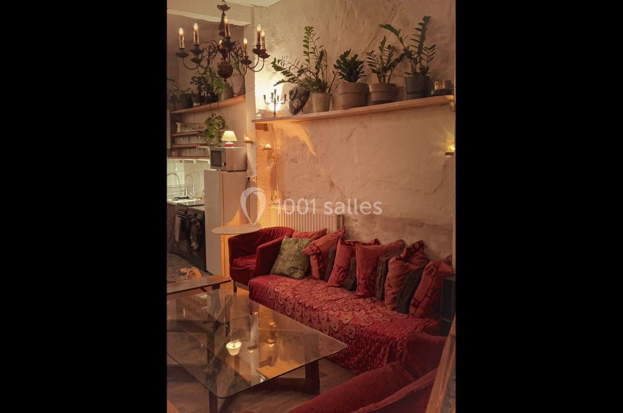 Salon chaleureux avec canapé rouge, coussins assortis, table basse en verre, étagères décorées de plantes et lumière tamisée.