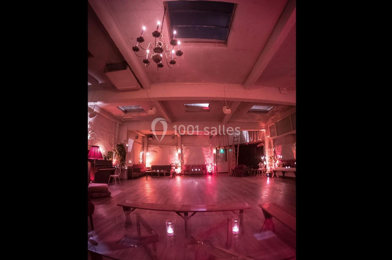 Salle spacieuse avec parquet, éclairage tamisé rose et lustre suspendu, ambiance chaleureuse et intime.