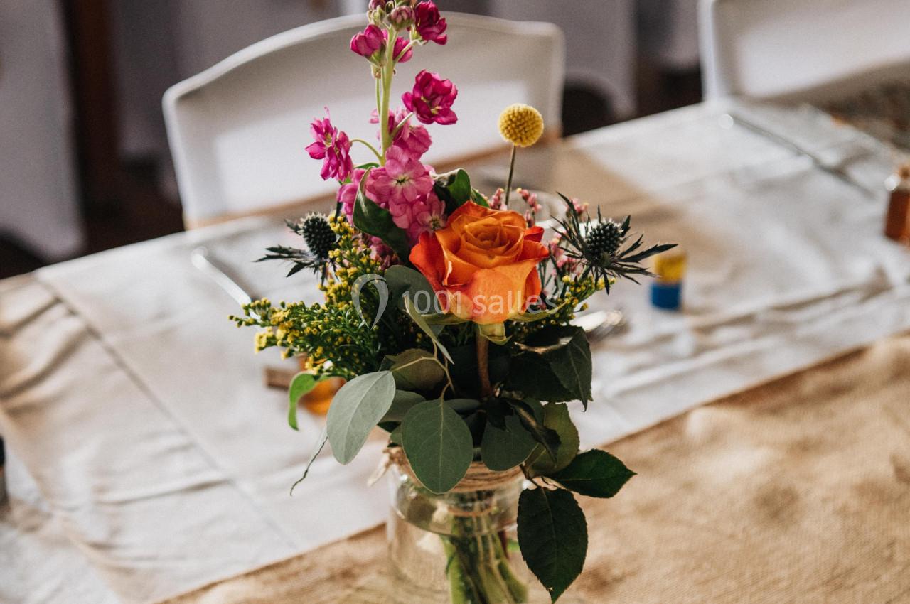 Centre de table avec un bouquet de fleurs colorées dans un vase en verre, posé sur une nappe en toile de jute.