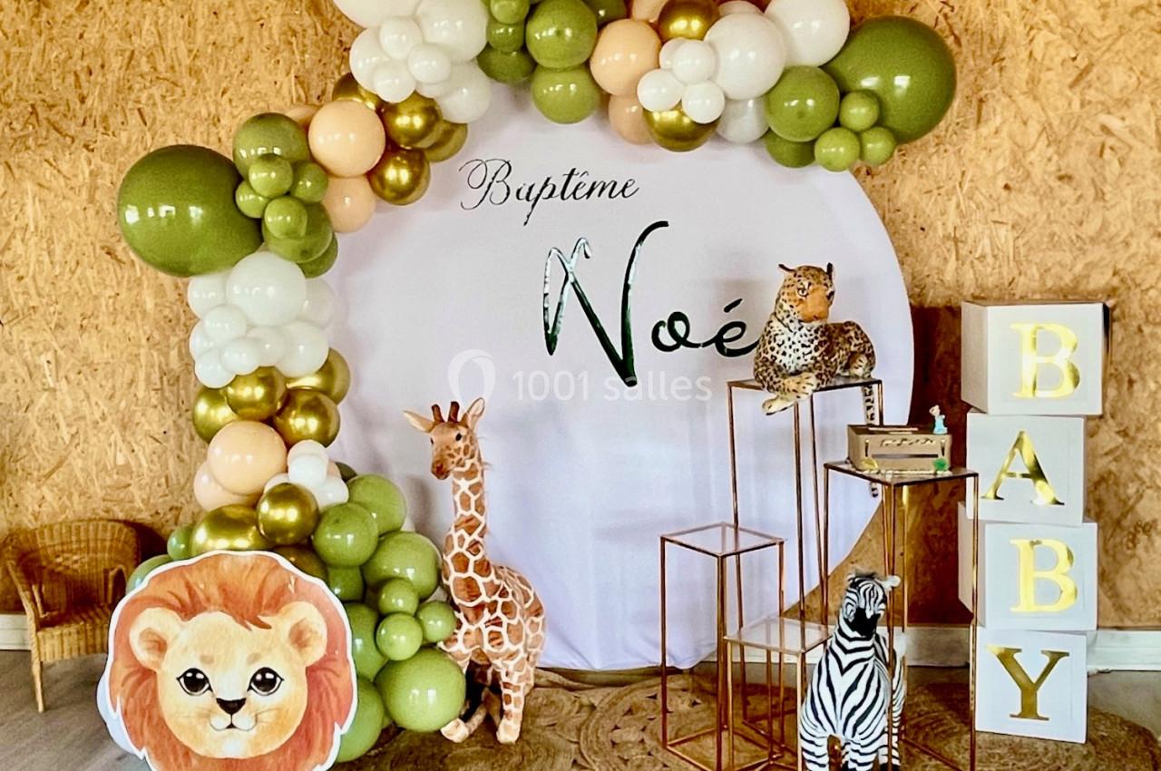 Décoration de baptême avec arche de ballons verts et blancs, animaux en peluche et cubes formant le mot ’BABY’.